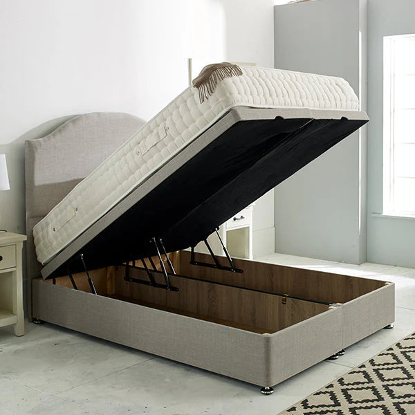Ottomans lift mechanism divan bed base in a silver plush velvet fabric with a wooden frame and footboard, shown in an open position to display the storage space inside.