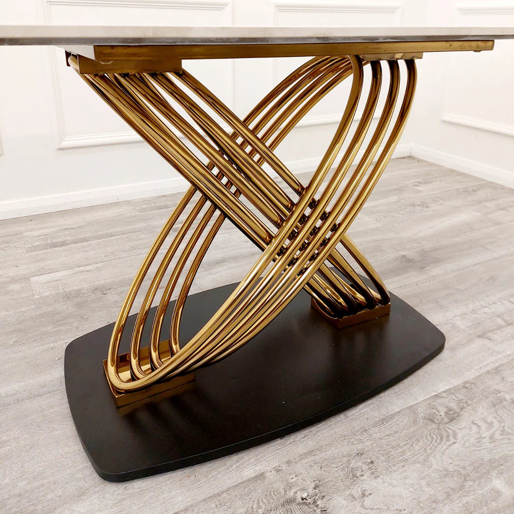 Modern dining table with gold metal base and marble top on a wooden floor.